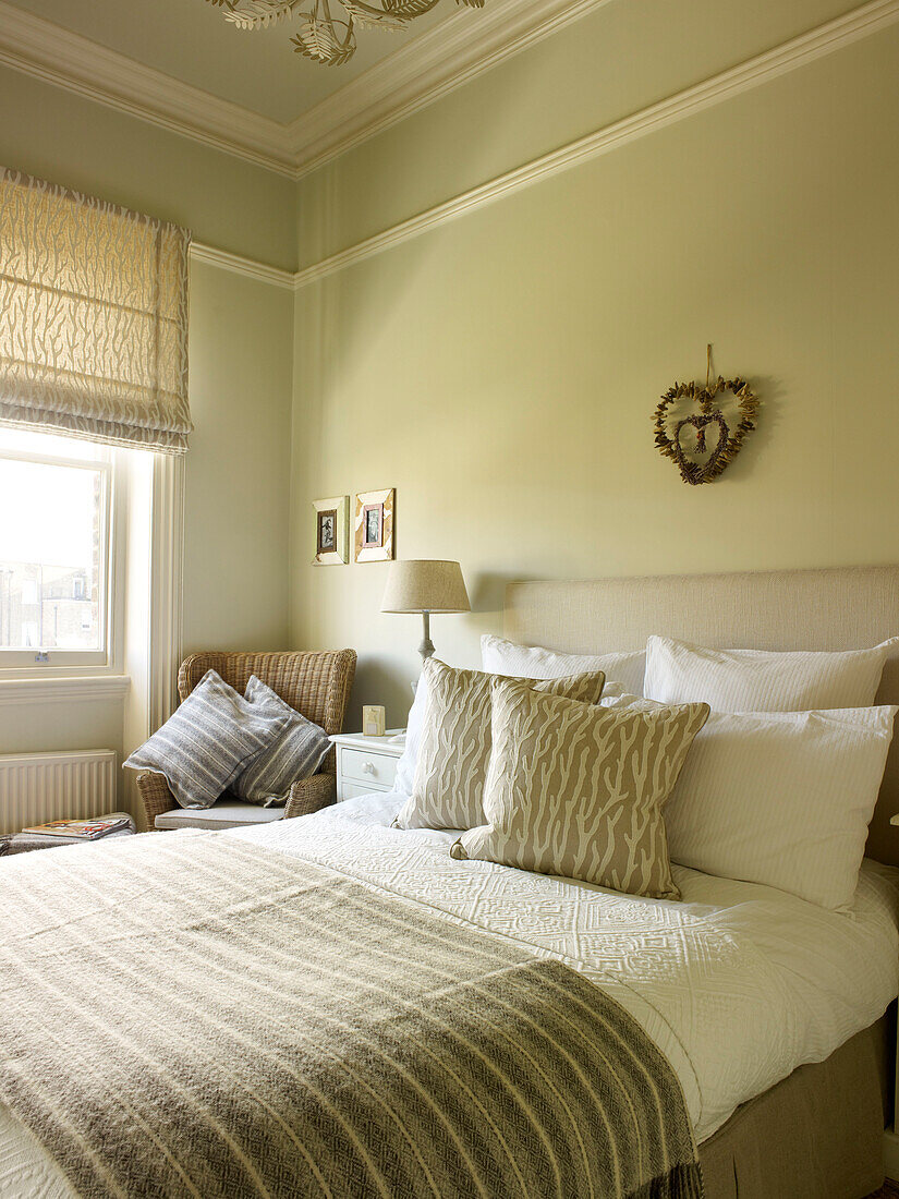 Gestreifte Decke auf einer Perle in einem Zimmer mit Korbstuhl am Fenster in einem Haus in Kensington, London, England, UK