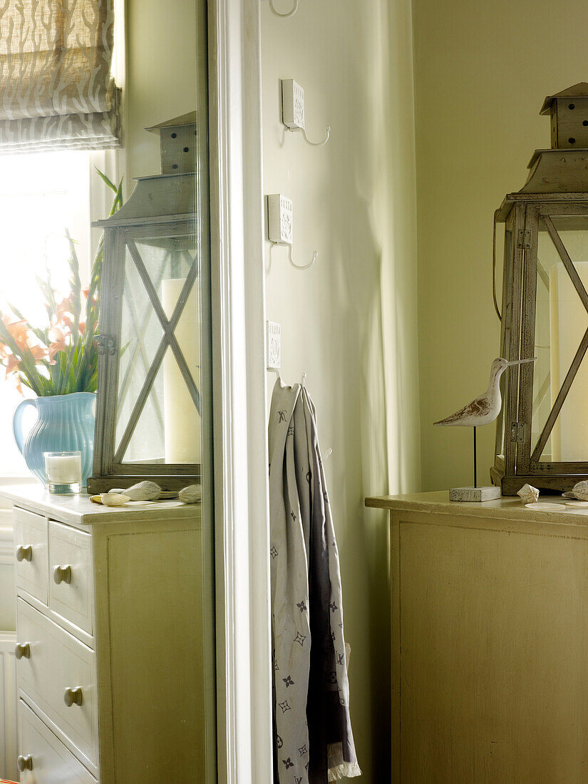 Spiegelung einer Kommode mit Sturmlaterne im Schlafzimmerspiegel in einem Haus in Kensington, London, England, UK