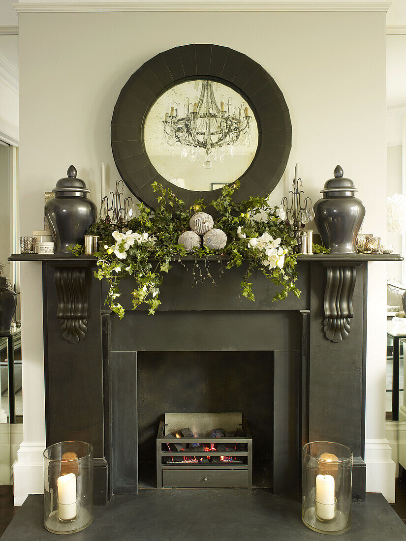 Christmas garlands on black fireplace with circular mirror and urns in London home England UK