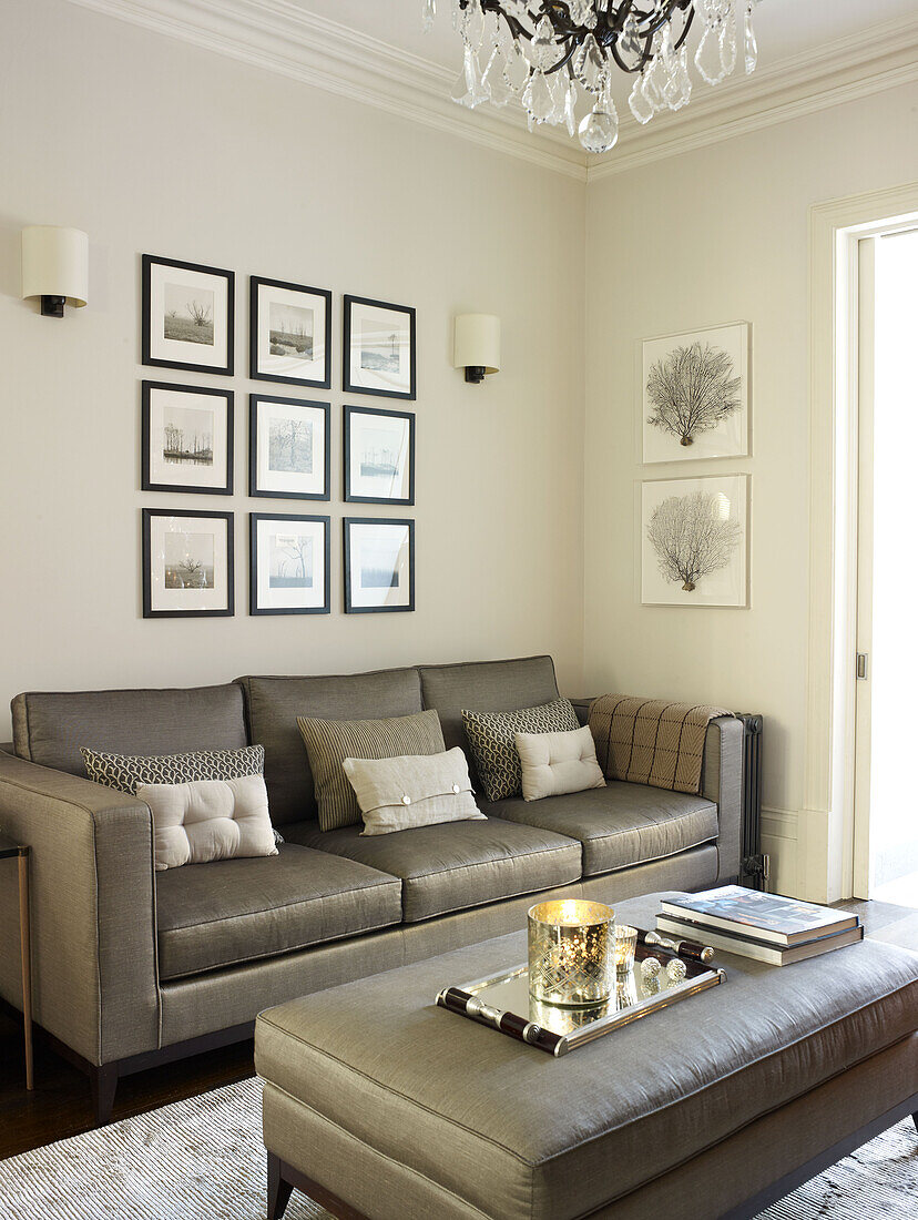 Beleuchtete Kerze auf einer silbernen Ottomane im Wohnzimmer mit grauem Sofa und Kunstwerken in einem klassischen Londoner Haus England UK