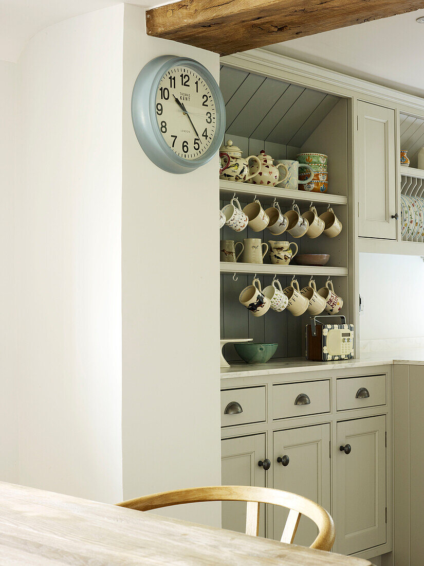 Uhr und Küchenkommode mit Tassen in einer Bauernhausküche in West Sussex, England, Vereinigtes Königreich
