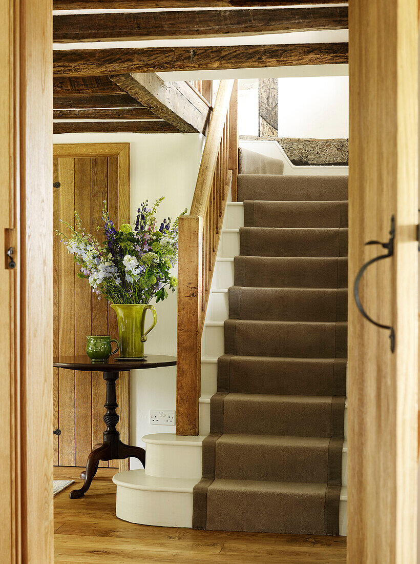 Wooden banister and cut flowers with brown carpeted staircase in West Sussex farmhouse, England, UK