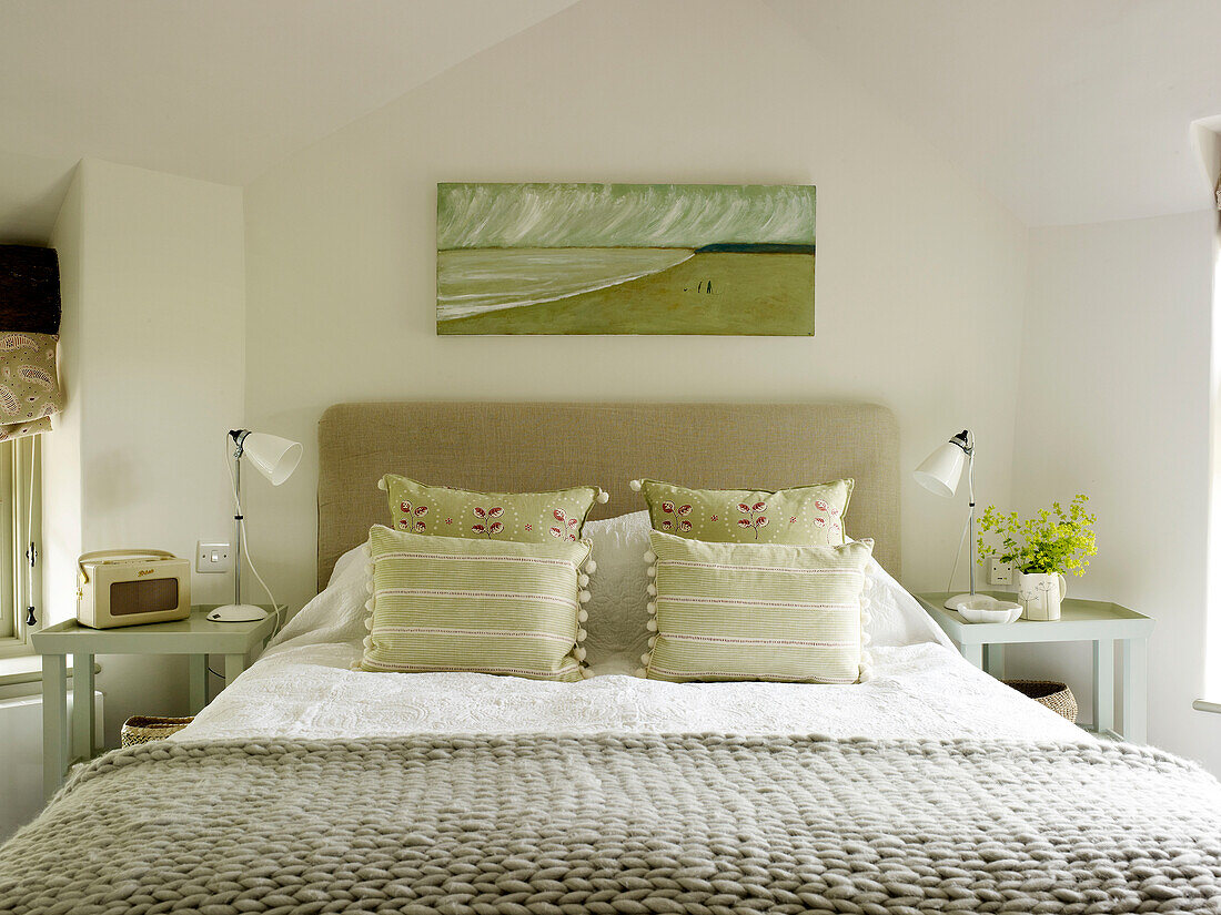 Leinwand über einem Doppelbett mit hellgrünen Kissen und Wolldecke in einem Bauernhaus in West Sussex, England, Vereinigtes Königreich