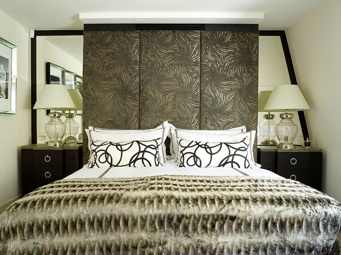 Glass lamps at bedside with large fabric covered headboard in London townhouse, UK