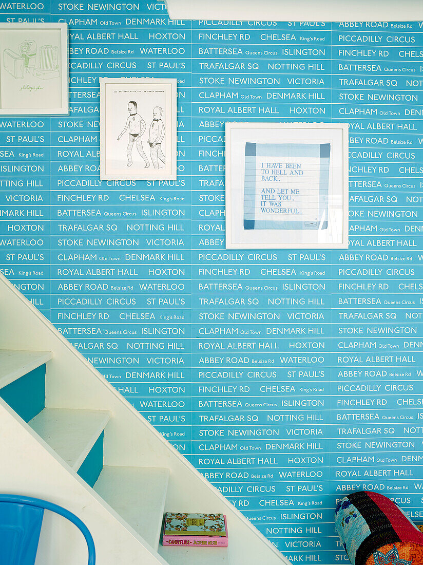 Framed prints on bright blue staircase wallpaper in London family home, UK