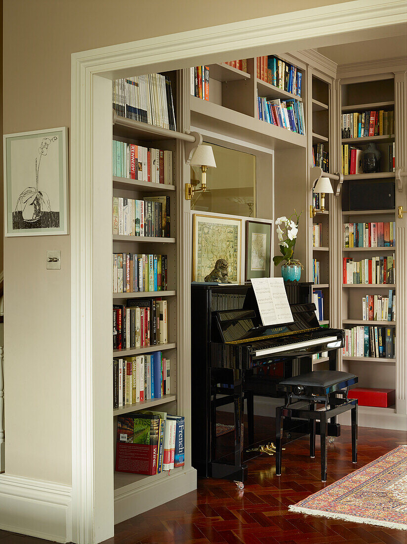 Klavier und Bücherregale in einer Bibliothek mit poliertem Parkettboden in einem Londoner Stadthaus, Vereinigtes Königreich