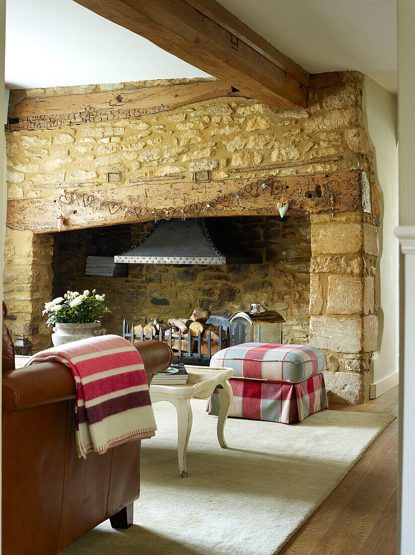 Karierter Hocker mit freiliegendem Steinherd und gestreifter Decke über einem Sessel in einem Cottage in Oxfordshire, England, UK