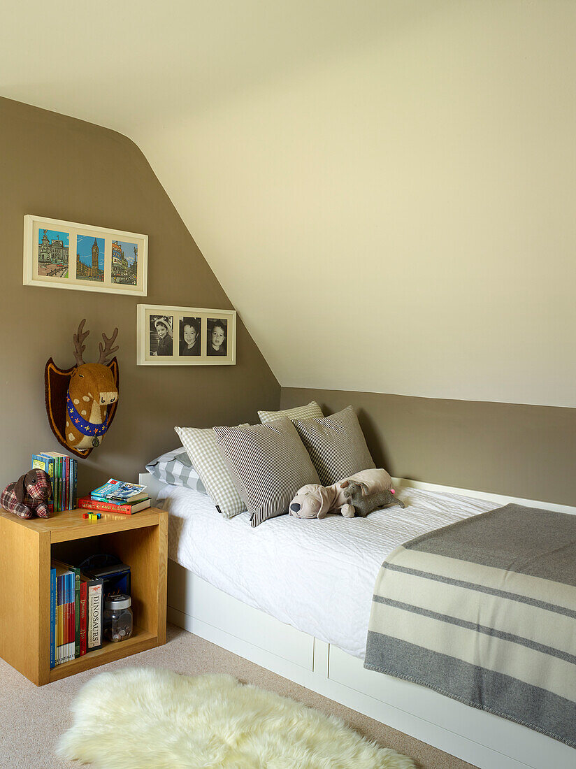 Soft toys on single bed with wooden side table and grey blanket in Oxfordshire cottage, England, UK