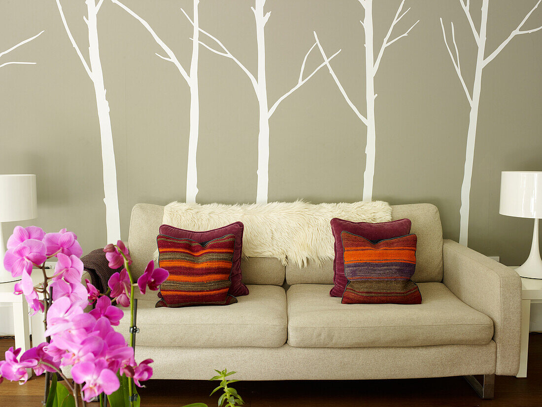 Gestreifte Kissen auf Sofa mit Baum-Wanddekoration und rosa Orchidee in einem Londoner Haus, UK