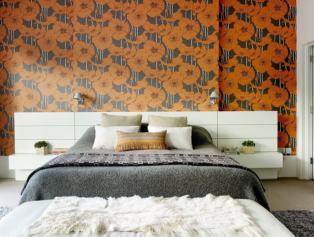White fur on lounger at foot of double bed with orange floral wallpaper in London home, UK