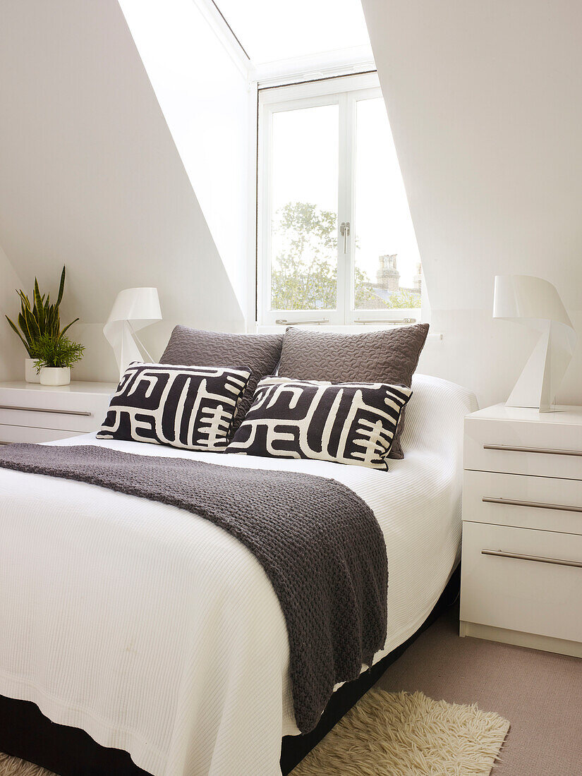 Black patterned pillows on double bed below dormer window of London home, UK