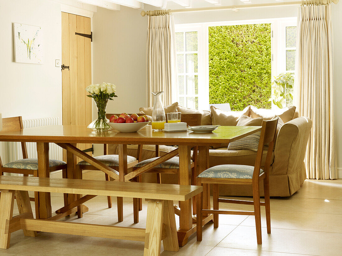 Esstisch und Stühle aus Holz mit Sofa und offenen Terrassentüren in einem Haus in Nottinghamshire England UK