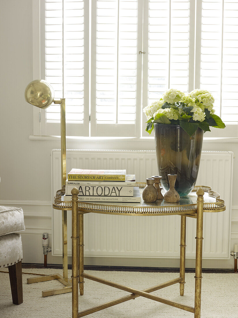 Vase of hydrangeas and books on vintage side table with lamp in North London townhouse England UK