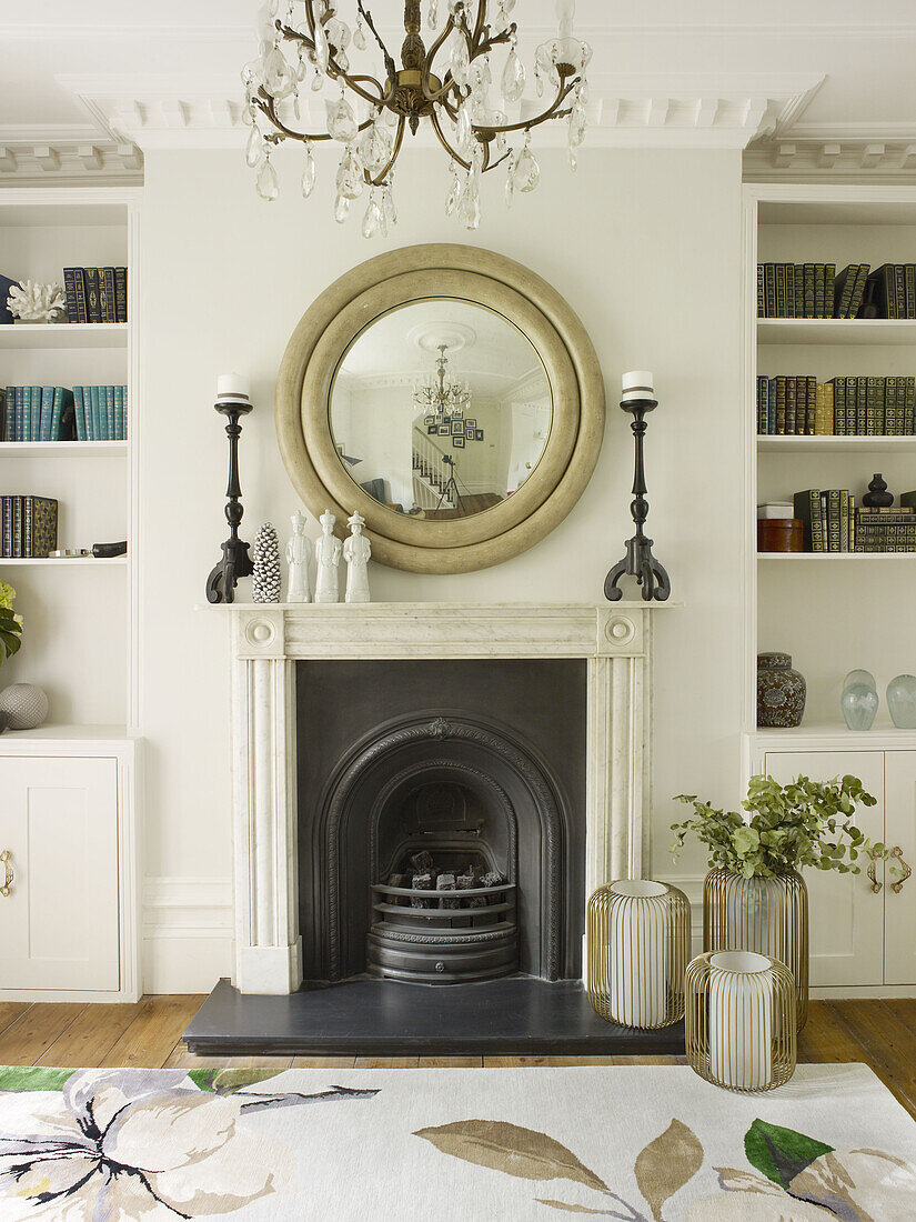 Circular mirror above fireplace with bookshelves in living room of North London townhouse England UK