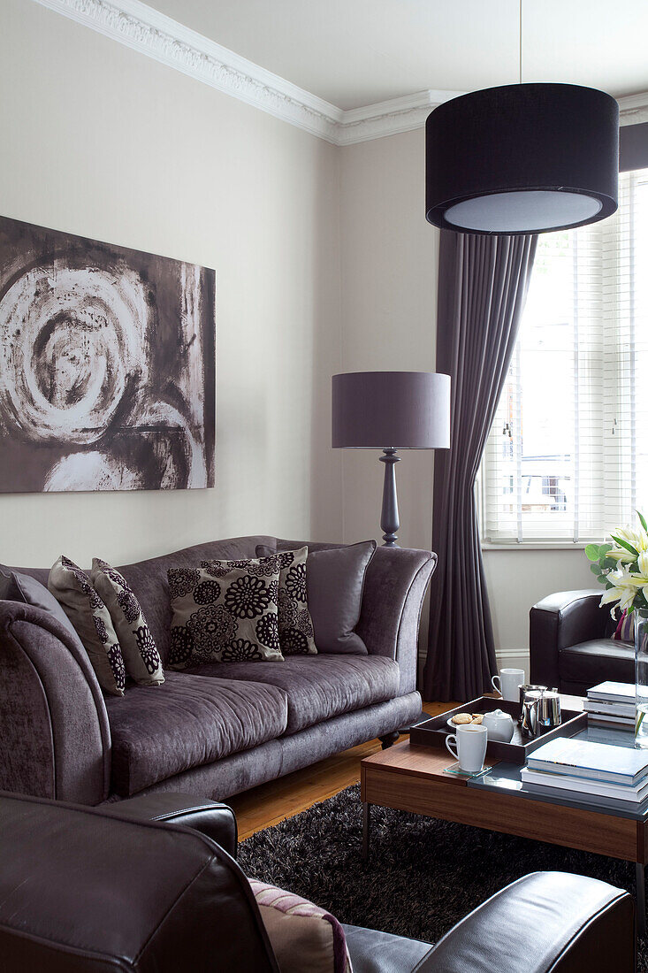 Gedecktes graues Sofa und Lampen mit Kunstwerken im Wohnzimmer eines zeitgenössischen Hauses in London, England, Vereinigtes Königreich