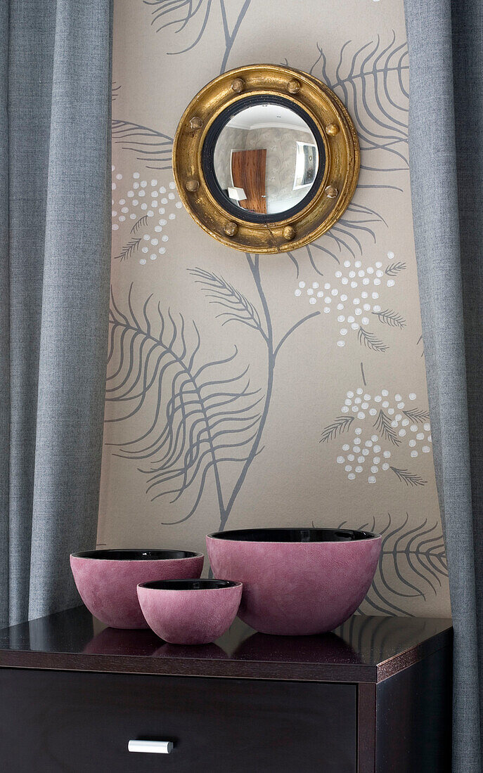 Pink bowls on sideboard under porthole mirror