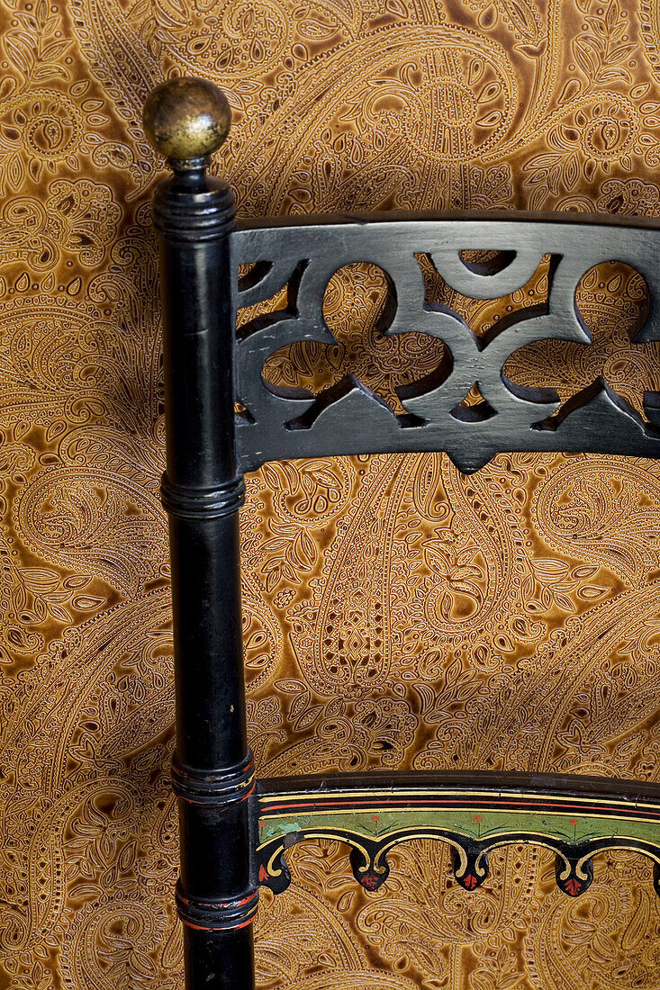 Carved black chair back and brown patterned wallpaper