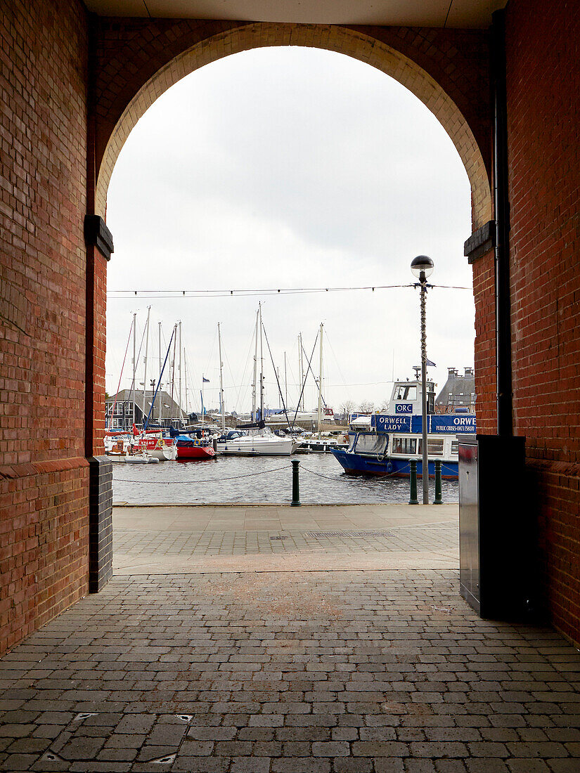 Blick durch eine gewölbte Backsteingasse auf vertäute Boote im Hafen von Ipswich, Suffolk, England, UK