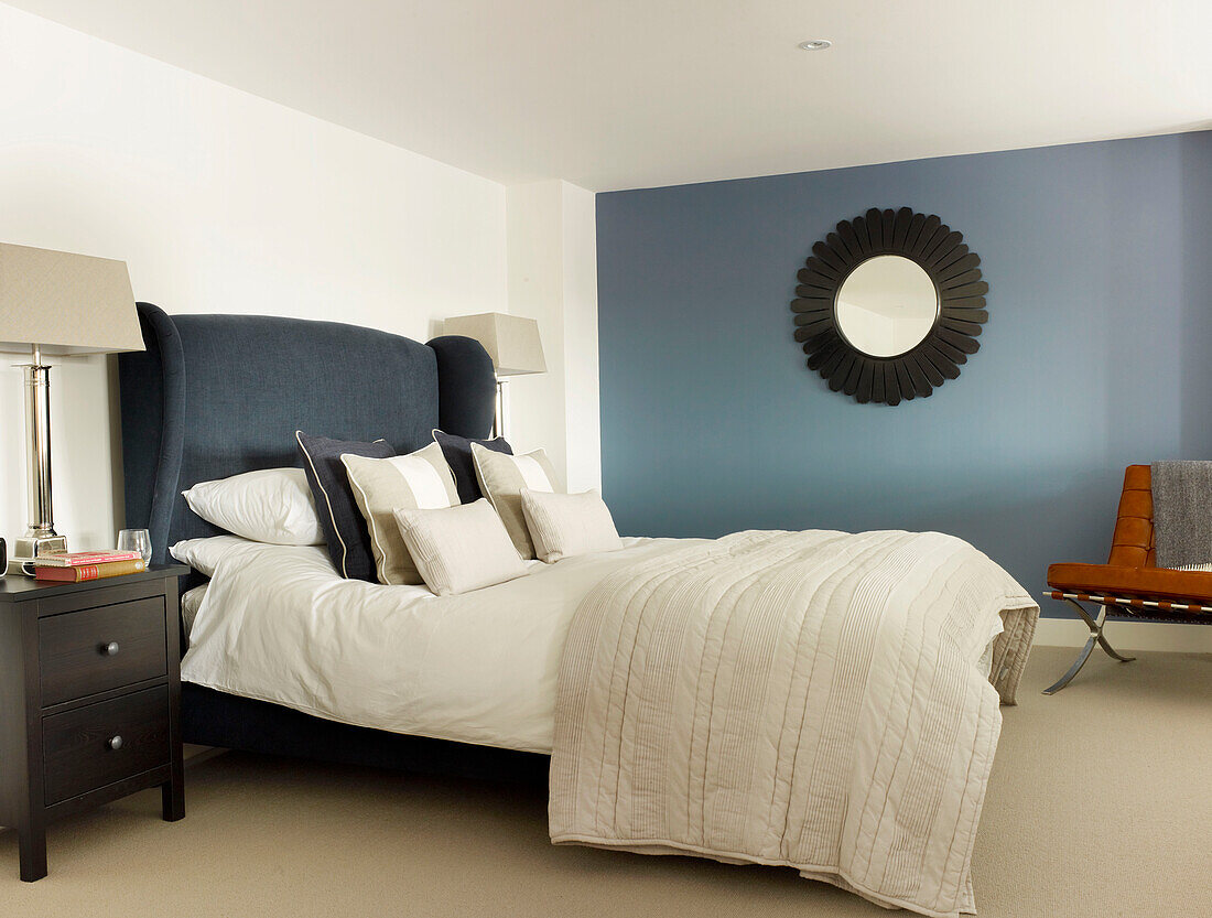 Blue velvet headboard with cream quilts and mirror in bedroom of Ipswich warehouse conversion, Suffolk, England, UK