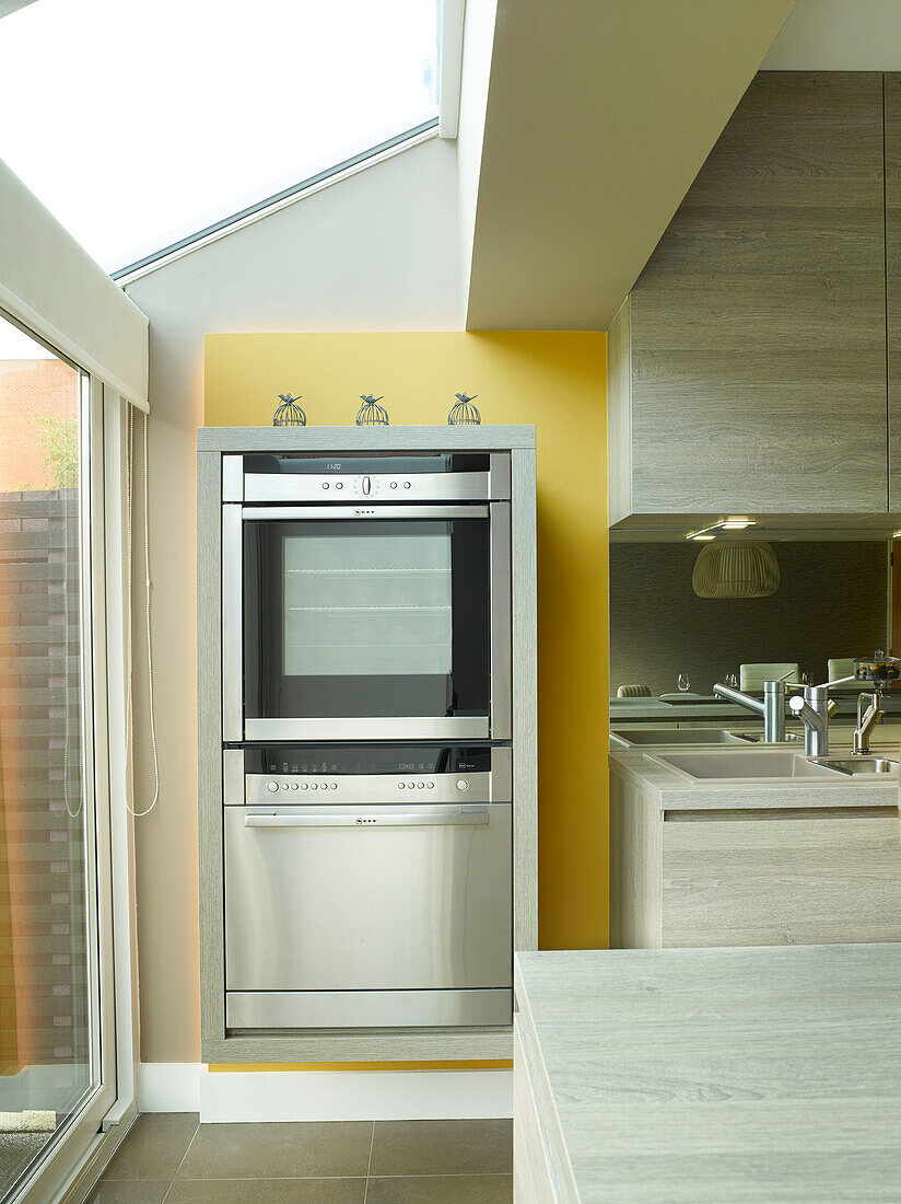 Stainless steel double oven on yellow panel in kitchen of Manchester home, England, UK