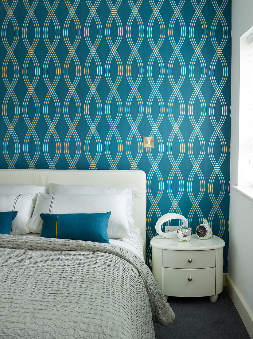 Blau gemusterte Tapete über dem Doppelbett mit weißem Beistelltisch in einer Wohnung in Manchester, England, UK