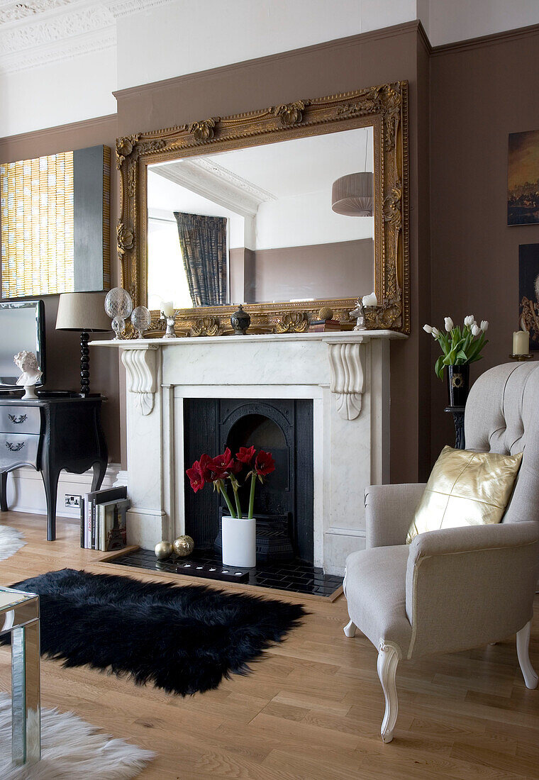 Vergoldeter Spiegel am Kamin mit Sessel im Wohnzimmer eines Hauses in Hove, East Sussex, Großbritannien