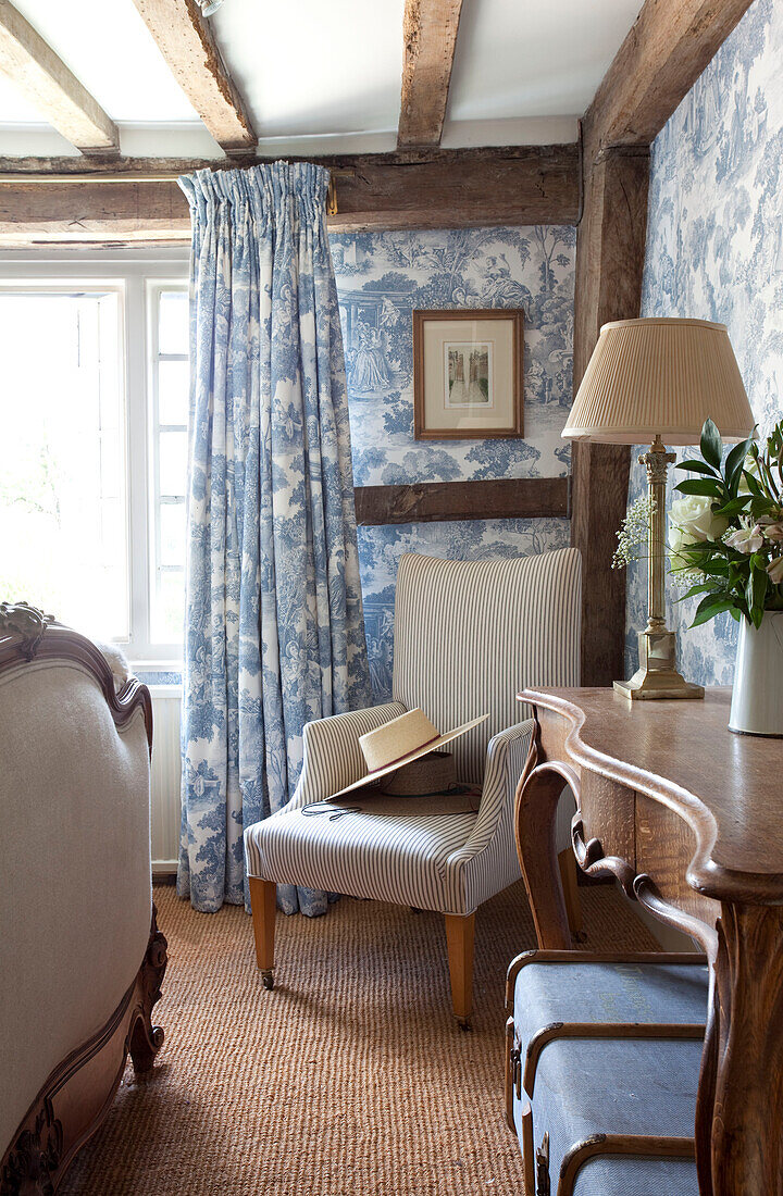Armchair in corner of timber framed cottage bedroom with toile wallpaper and curtains, Kent, England, UK