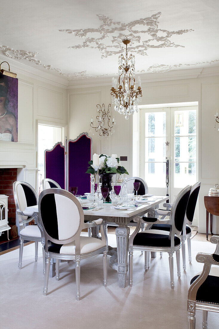 Schwarz-weiß gepolsterte Esszimmerstühle am Tisch unter dem Kronleuchter im Esszimmer mit lila Paravent