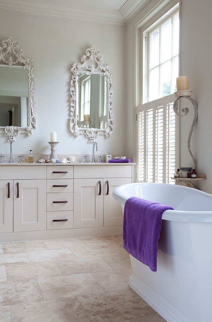 Freestanding bath with purple towel and ornate mirrors above washbasins in classic bathroom