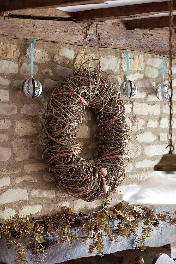 Natural Christmas wreath hanging with baubles on exposed stone wall in Cotswolds home UK
