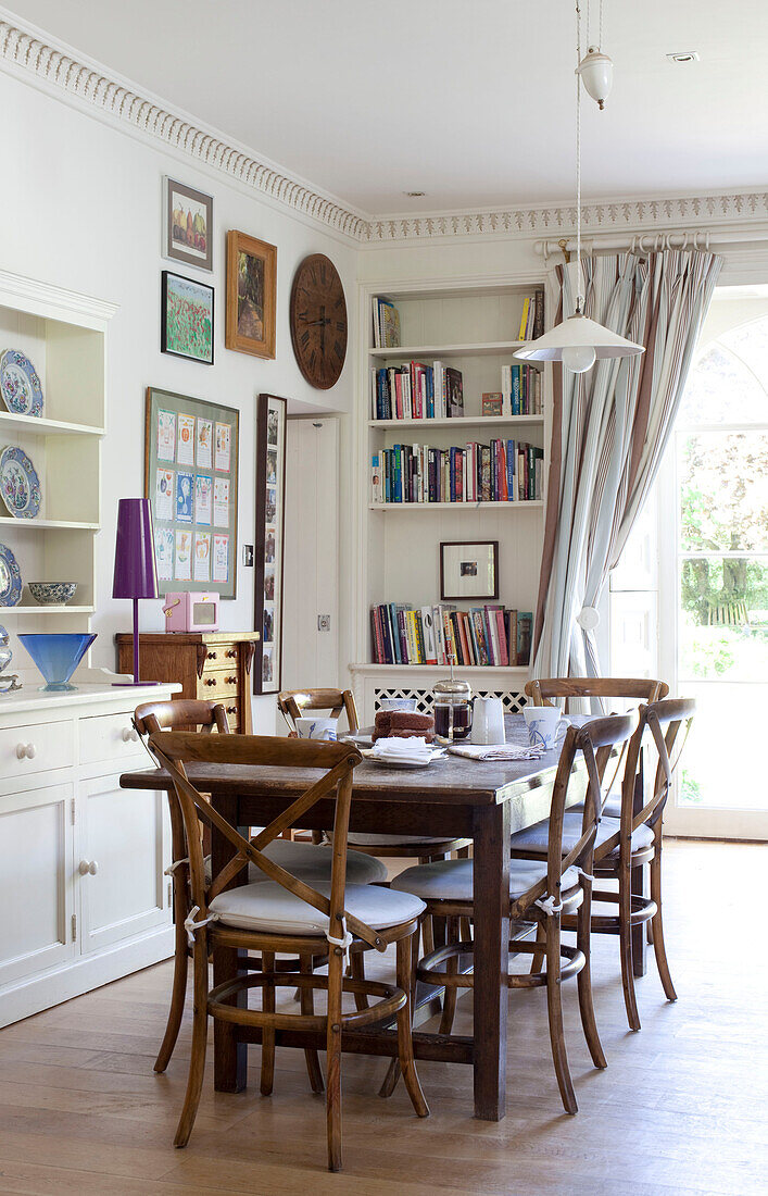 Wooden dining table and chairs with bookcase in East Sussex home, England, UK