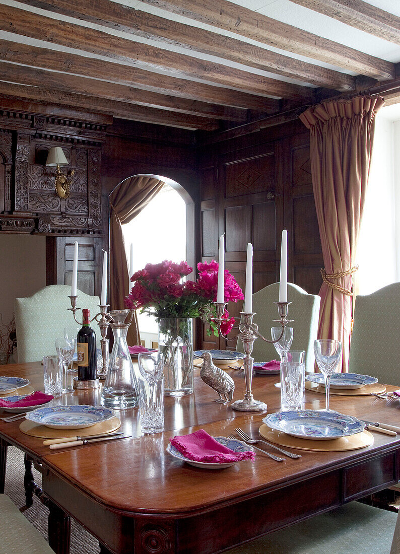 PInk flowers and place settings on polished antique dining table in East Sussex home, England, UK