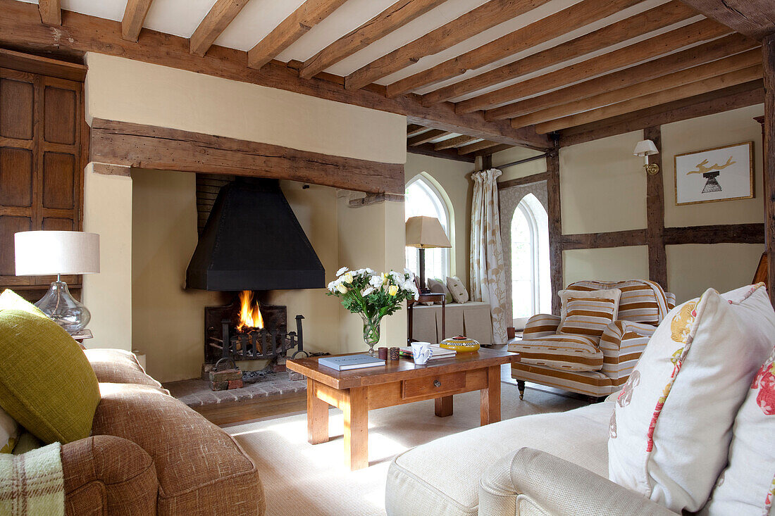 Befeuertes Feuer im Wohnzimmer mit Balkendecke in einem Haus in East Sussex, England, Vereinigtes Königreich