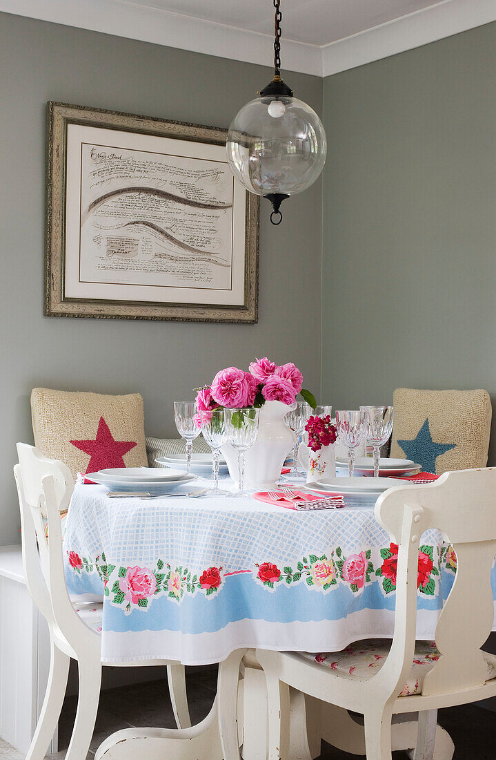 Floral tablecloth and wineglasses below glass pendant light in Kent home UK
