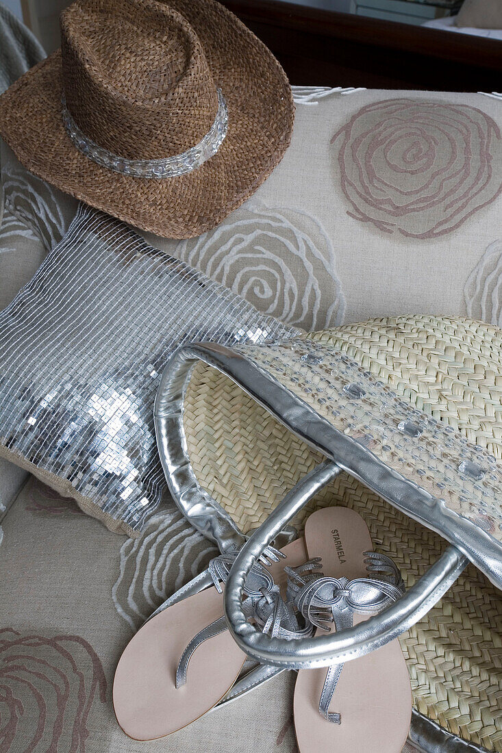 Silberne Flip-Flops und Kissen mit Sonnenhut und Tasche auf einem Sessel in einem Haus in London UK