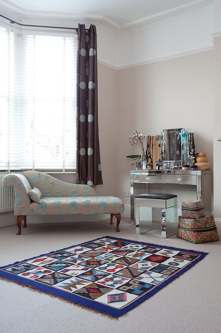 Upholstered chaise longue with mirrored dressing table and stool at window in contemporary London home, UK