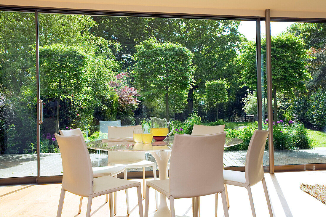 Tisch für sechs Personen an einem deckenhohen Fenster mit Blick auf den Garten in einem modernen Haus in London, England, Vereinigtes Königreich