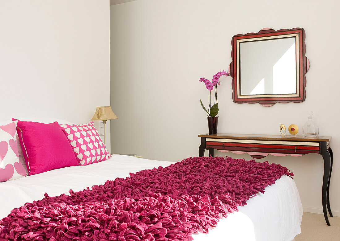 Quadratischer Spiegel und Beistelltisch im Schlafzimmer mit rosafarbener Bettdecke in einem Haus in Newmarket, Suffolk, Großbritannien