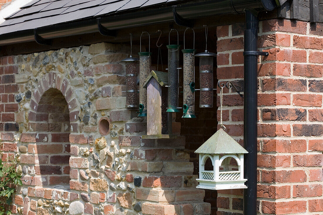 Vogelfutterspender und Vogelhäuschen hängen unter der Dachrinne an der Stein- und Ziegelfassade eines Hauses in Suffolk UK