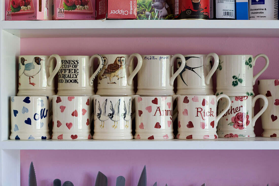 Tassen und Teesortiment auf einem Regal in der rosa Küche eines Hauses in Suffolk, UK