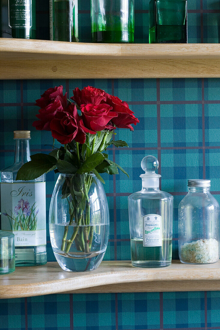Vase mit roten Rosen auf Regal mit Flaschen vor türkisfarbener Karotapete in Suffolk UK