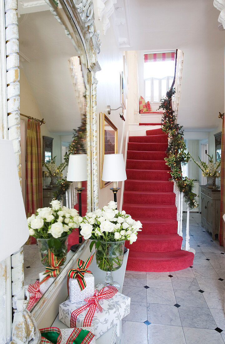 Treppe mit rotem Teppich in einer weißen Eingangshalle mit Weihnachtsdekoration in einem Haus in London, UK