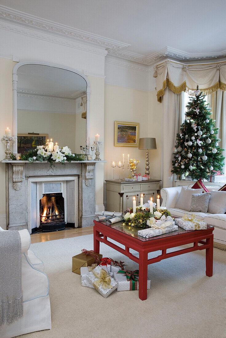 Christmas tree with giftwrapped presents and lit fire in London home UK