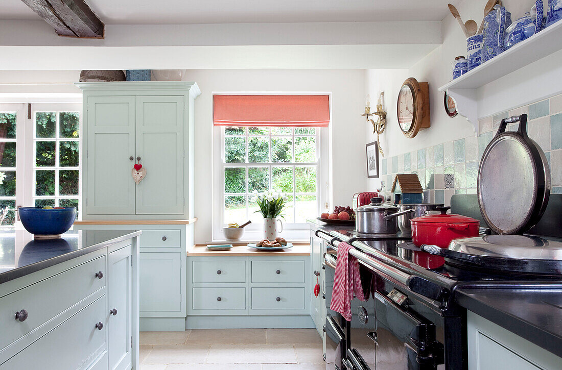 Saucepans on hob of range oven in pastel blue fitted kitchen of Sussex farmhouse, UK