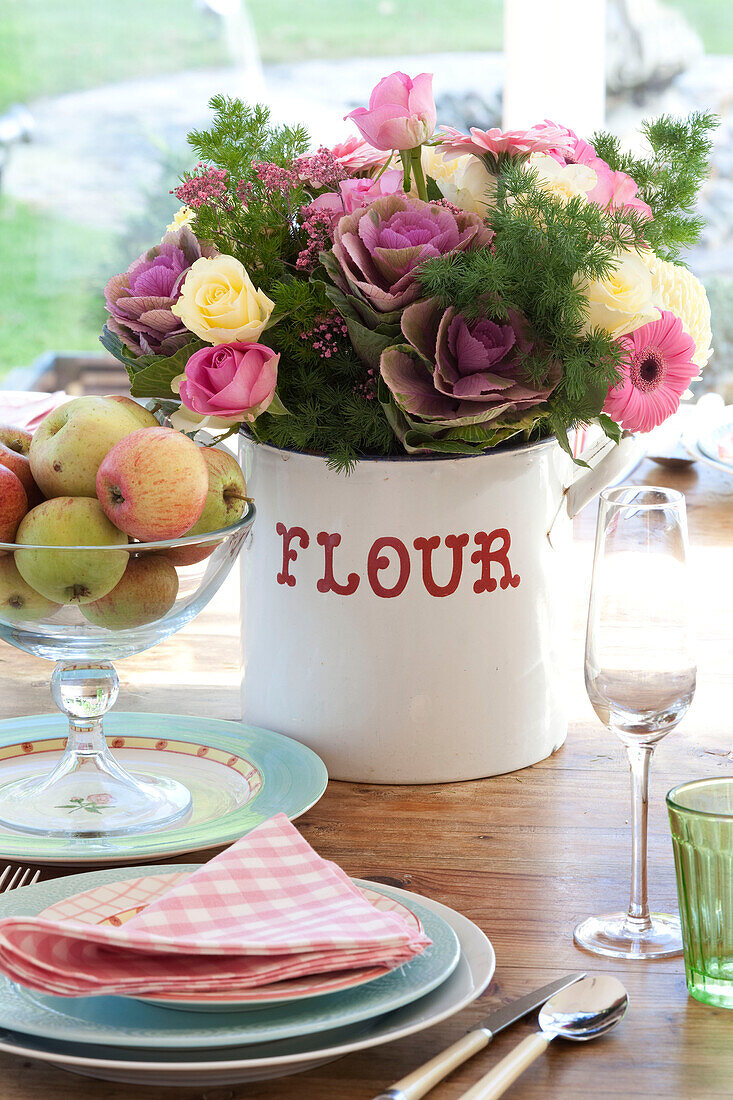 Cut flowers in flour bin with pace setting and bowl of apples in Berkshire home, England, UK