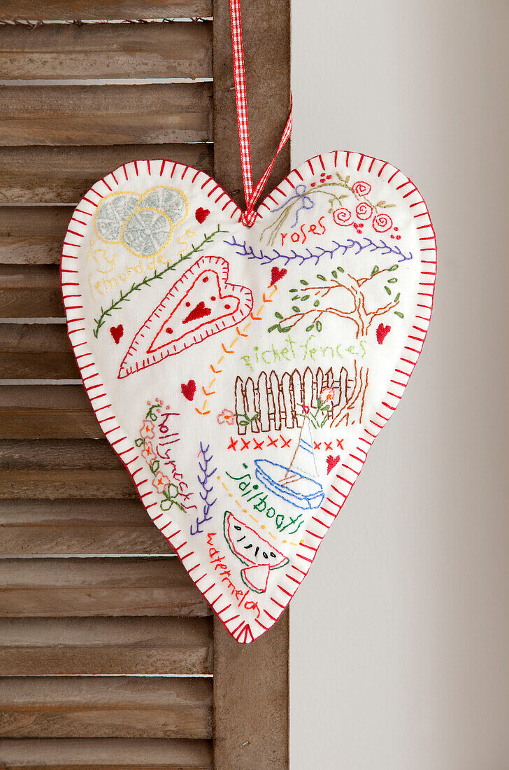Hand embroidered love heart hanging on louvered door in Berkshire home, England, UK