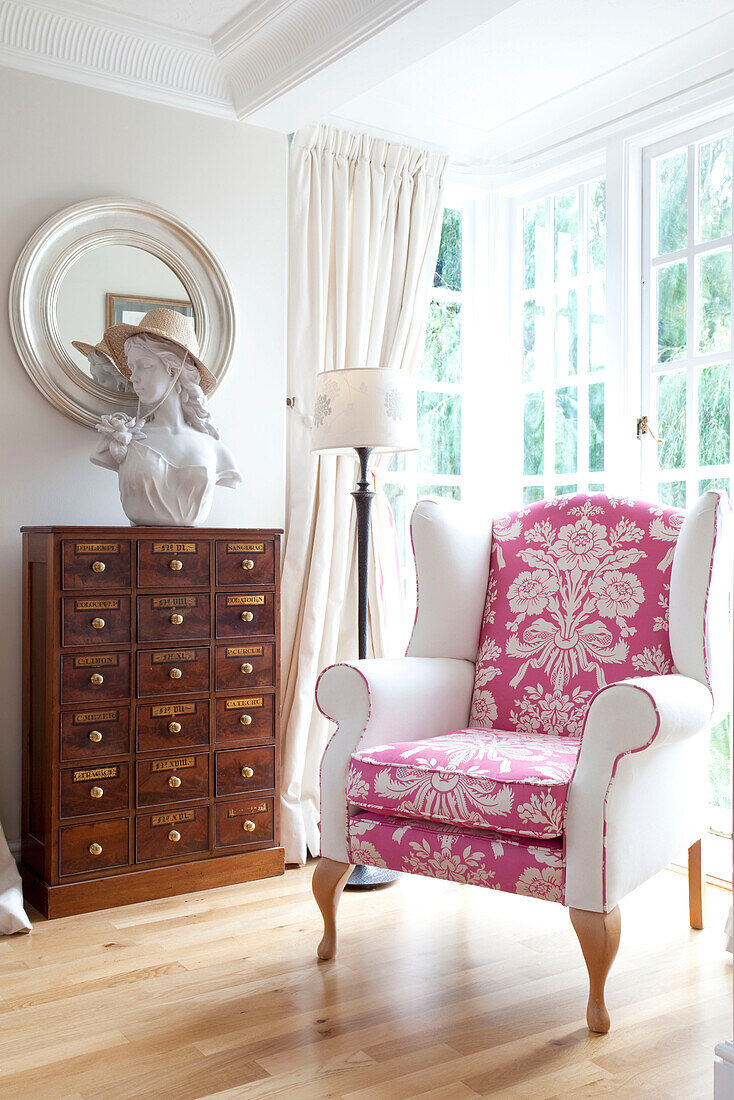 Vintage storage unit with pink and white upholstered wingback chair in Berkshire home, England, UK