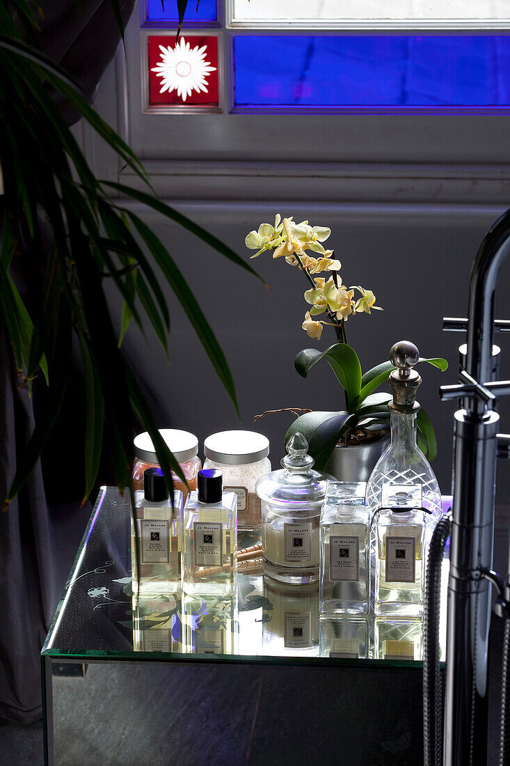 Glass toiletries and orchid in bathroom of contemporary London home, UK