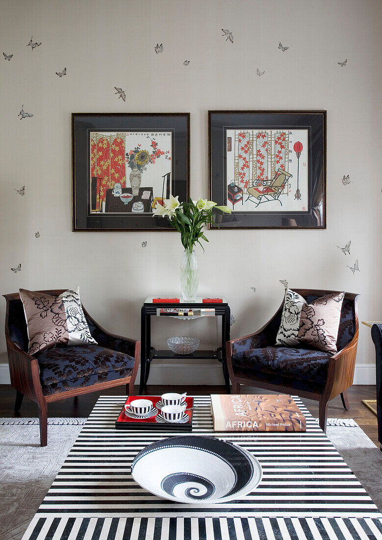 Matching armchairs and artwork in living room with black and white striped coffee tables in contemporary London townhouse, England, UK