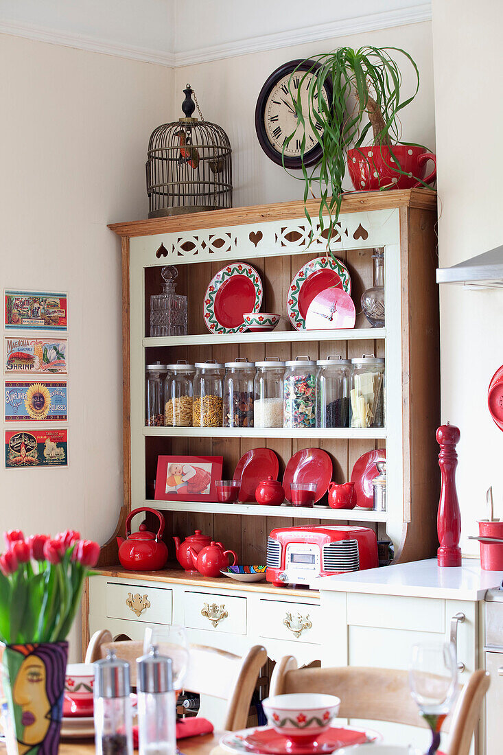 Birdcage on kitchen dresser with red crockery and storage jars in London townhouse, England, UK